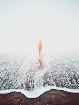 日出时分，薄雾笼罩的海滩上，一个神秘的剪影矗立在海浪之中