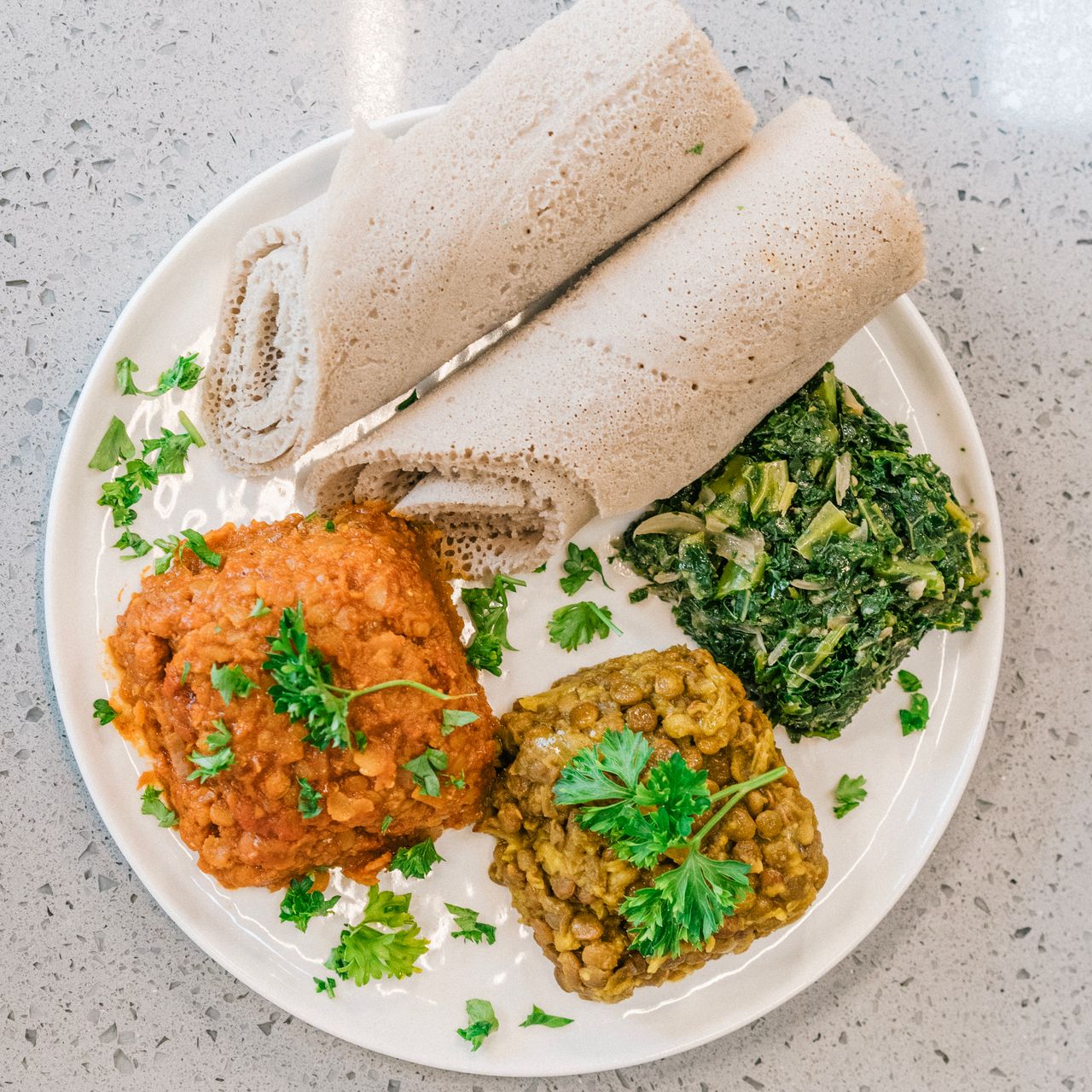 Ethiopian meal with injera flatbread and vibrant colorful stews arranged on a white plate