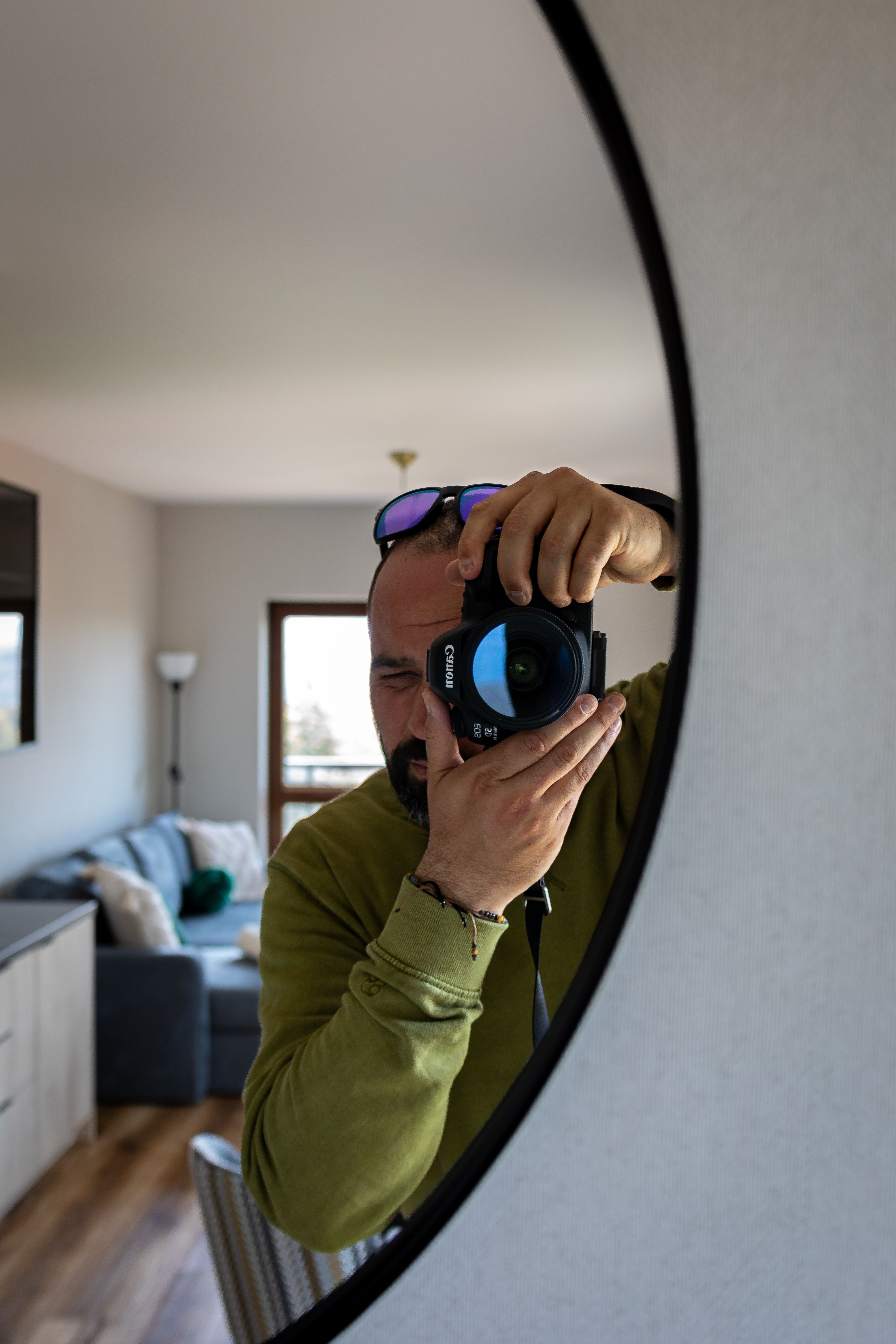 A man captures his reflection with a camera in a stylish indoor setting.
