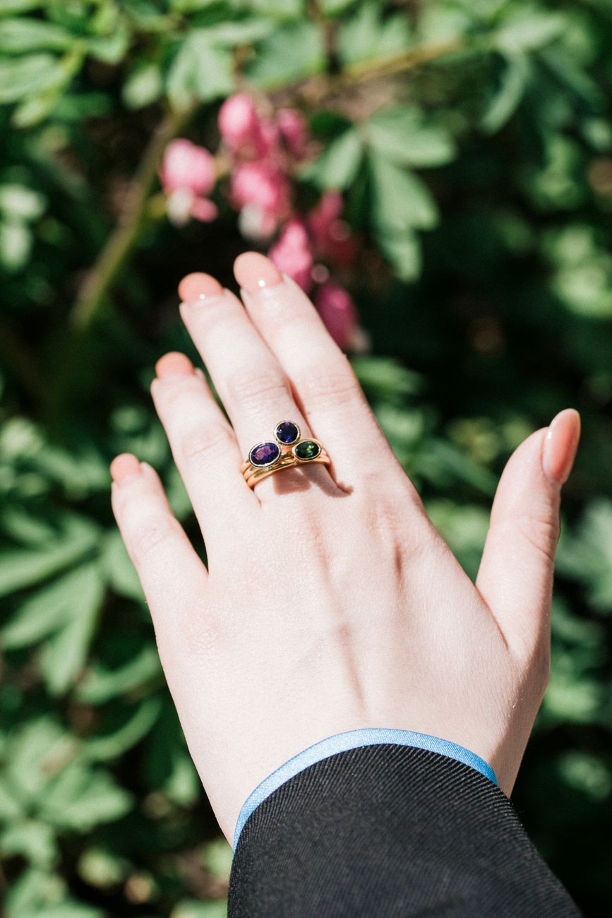 An elegant woman's hand adorned with a gemstone ring amidst lush garden foliage, capturing luxury and nature's beauty.