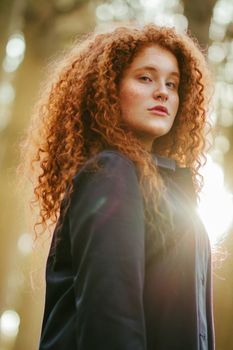 A captivating portrait of a redhead woman with curly hair, basking in sunlight.