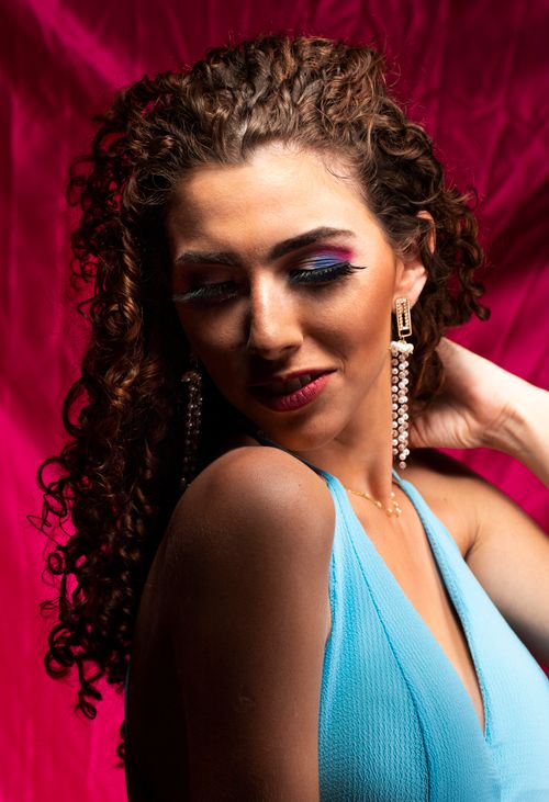 Free Stylish woman in blue dress with bold makeup and curly hair, set against a vibrant red background. Stock Photo