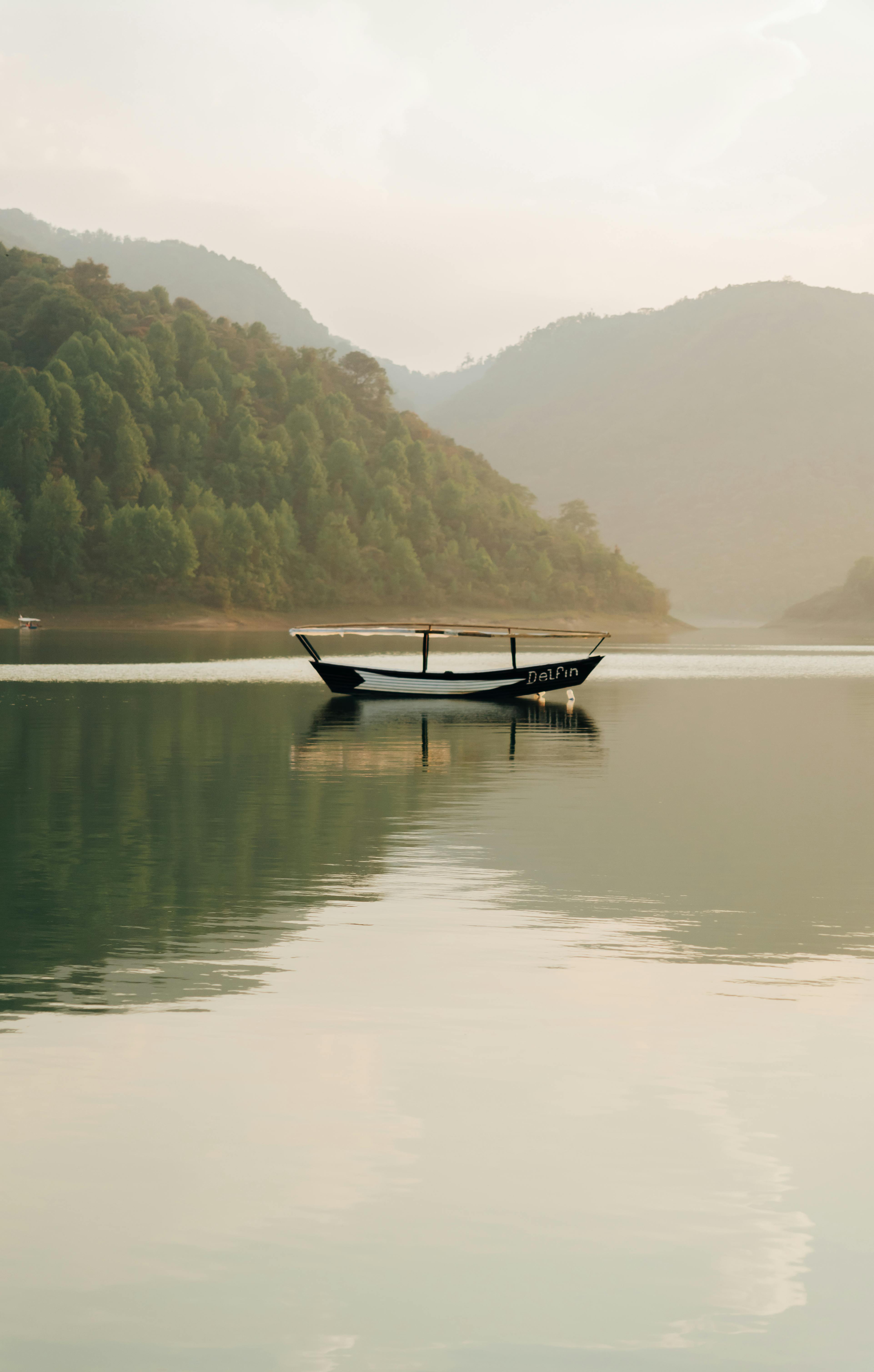 Serene landscape of a boat on a calm lake surrounded by hills and forest in Tenango de las Flores, Mexico.