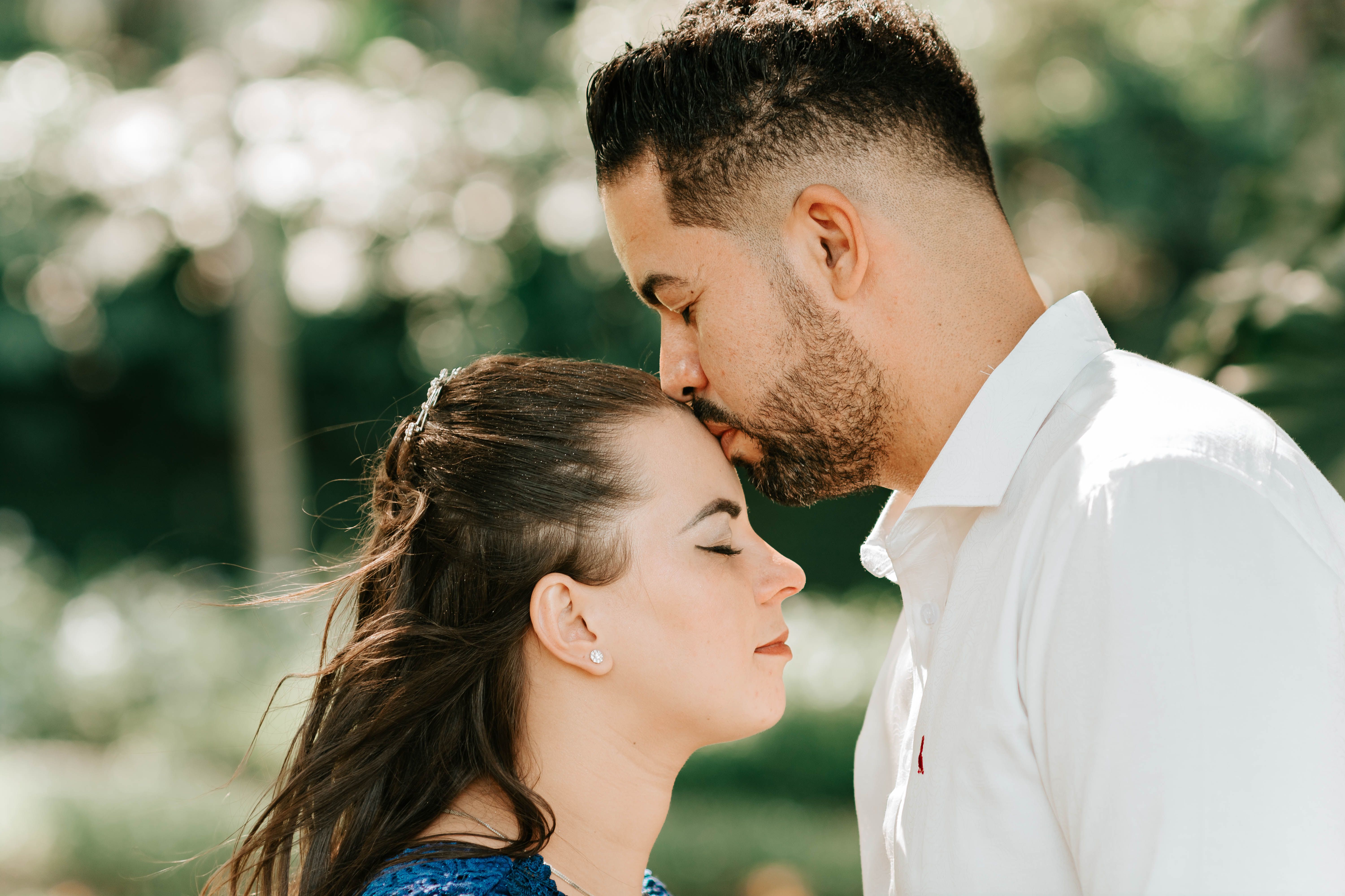 A loving couple shares an intimate forehead kiss amidst a serene outdoor setting.
