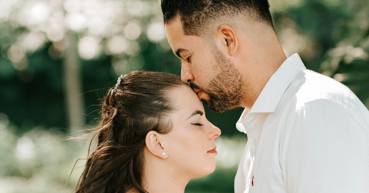 A loving couple shares an intimate forehead kiss amidst a serene outdoor setting.