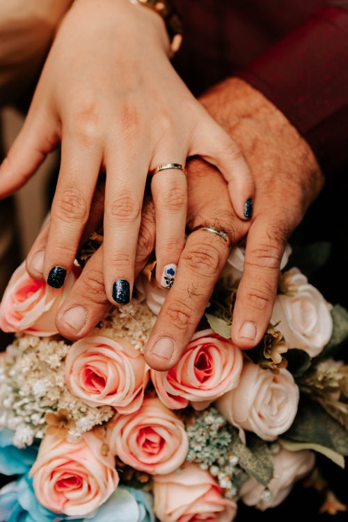 Free Close-up of bride and groom's hands with rings on a rose bouquet, symbolizing love and togetherness. Stock Photo