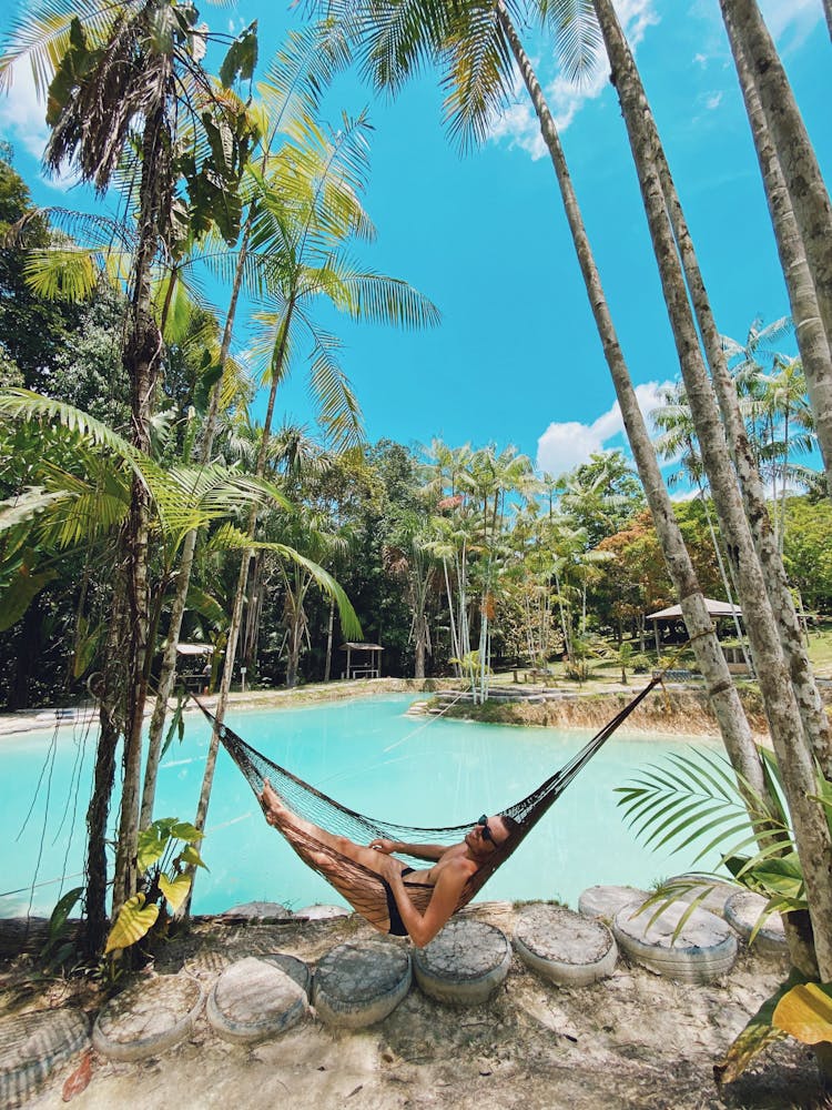 Woman Lying Down On Hammock Near Pond In Tropical Forest