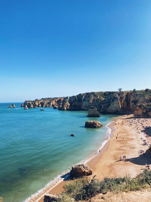 Free Discover a breathtaking beach with clear blue water and dramatic rocky cliffs under a bright sky. Stock Photo