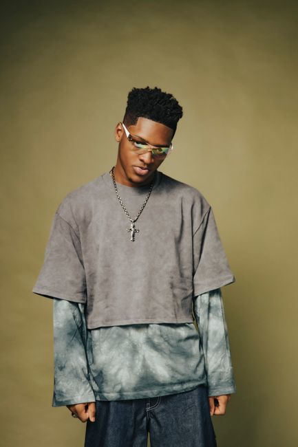 Stylish young man in layered outfit and sunglasses in fashion studio portrait.