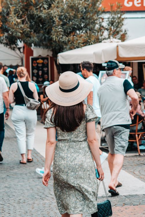 Free A woman in a floral dress and sun hat explores a lively outdoor market scene. Stock Photo