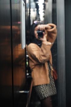 Blurred reflection of a woman taking a photo in an elevator mirror, creating an abstract effect.