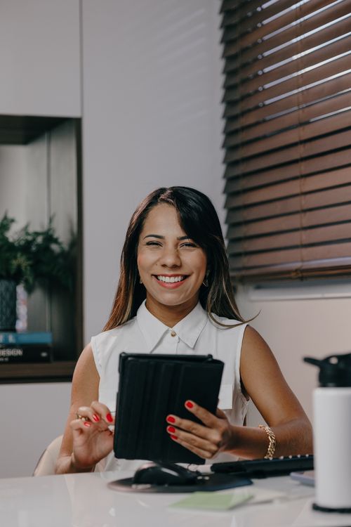 Free Happy woman with long hair smiling and holding a tablet while sitting indoors. Stock Photo