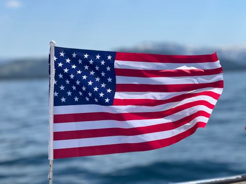 Free The United States flag waves on a bright day over the calm water. Stock Photo