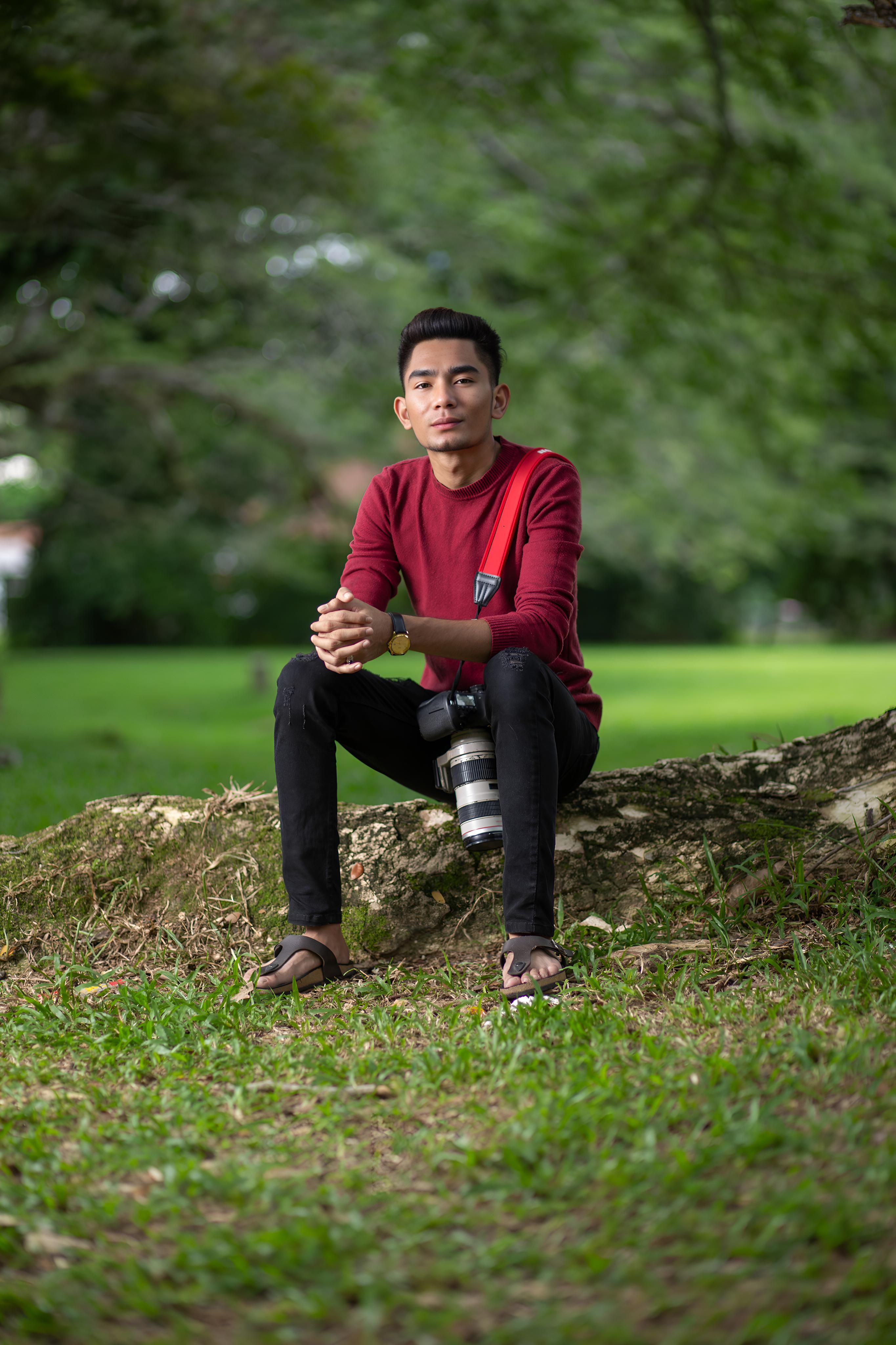 Portrait of a young man sitting on a tree trunk in a lush green park.