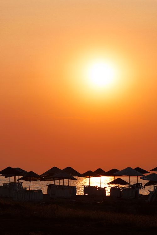 Free Captivating silhouettes of beach umbrellas against a vibrant sunset over the ocean. Stock Photo