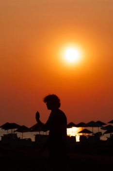 A captivating silhouette of a man walking on a beach at sunset with sun umbrellas in the background.