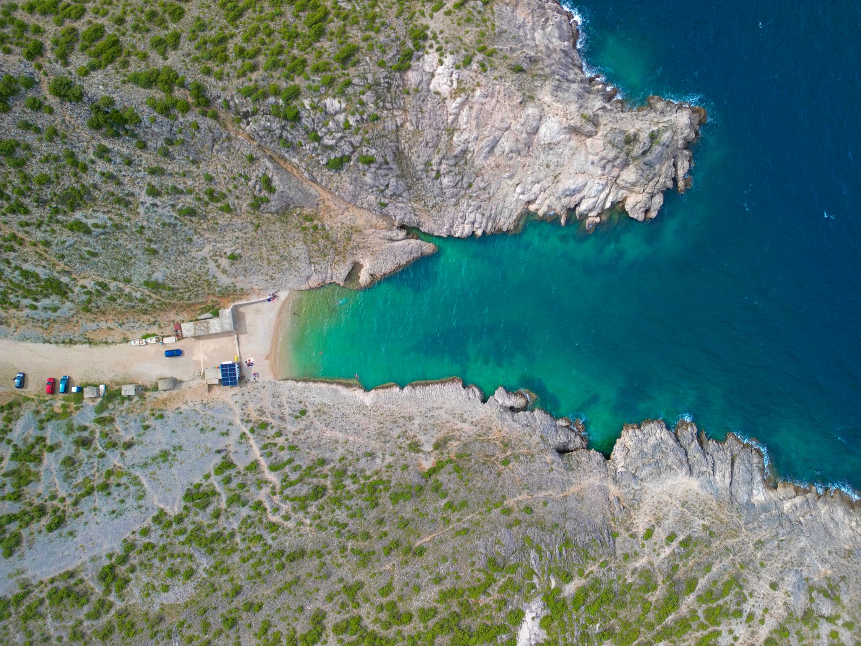 A breathtaking aerial view of a turquoise cove in Vrsi, Croatia, surrounded by rugged cliffs.