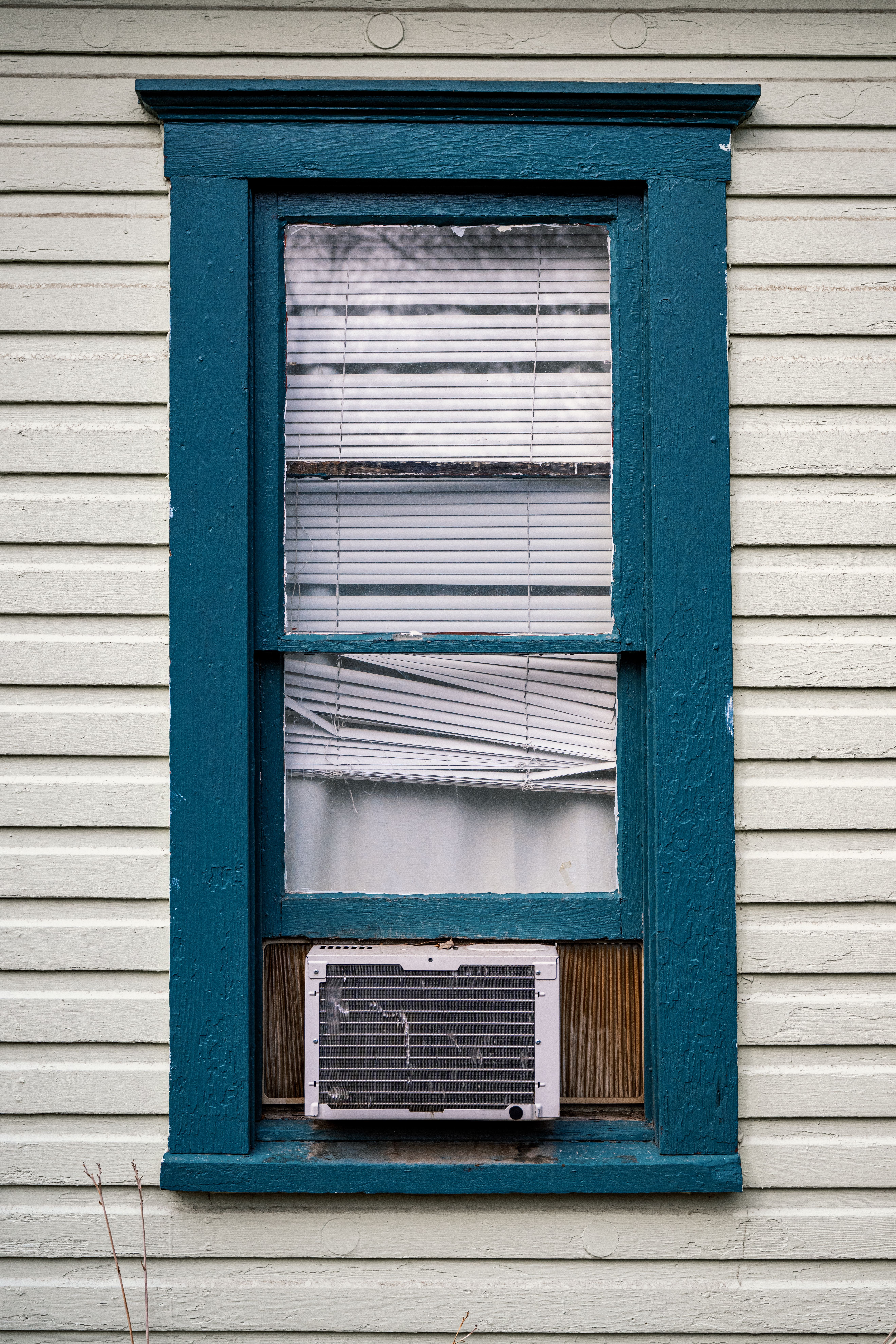 Close-up of a vintage wooden window with blue frame and air conditioner.