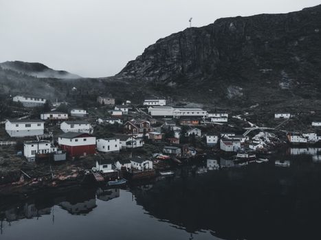 Picturesque rural village nestled by a lake under overcast skies, surrounded by mountains.