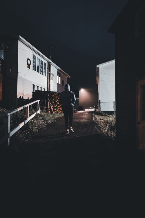 Free A solitary figure walking in a moody, illuminated street scene at night, evoking mystery. Stock Photo