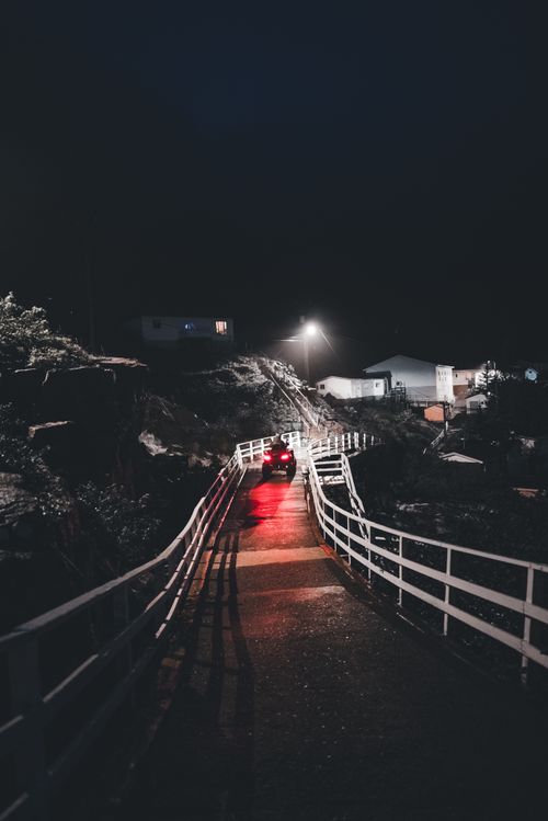 Free Moody nighttime street view with car headlights and railings under streetlights in a rural setting. Stock Photo