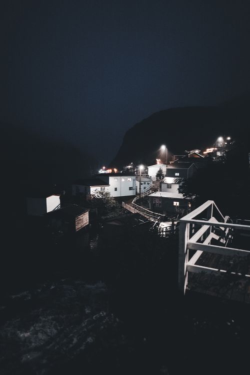 Free Illuminated fishing village at night with a serene atmosphere, highlighting quaint architecture and surrounding fjords. Stock Photo