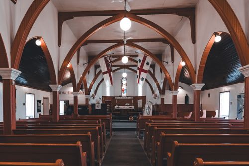 Free Beautiful interior view of a historic wooden church with arches, pews, and stained glass window. Stock Photo