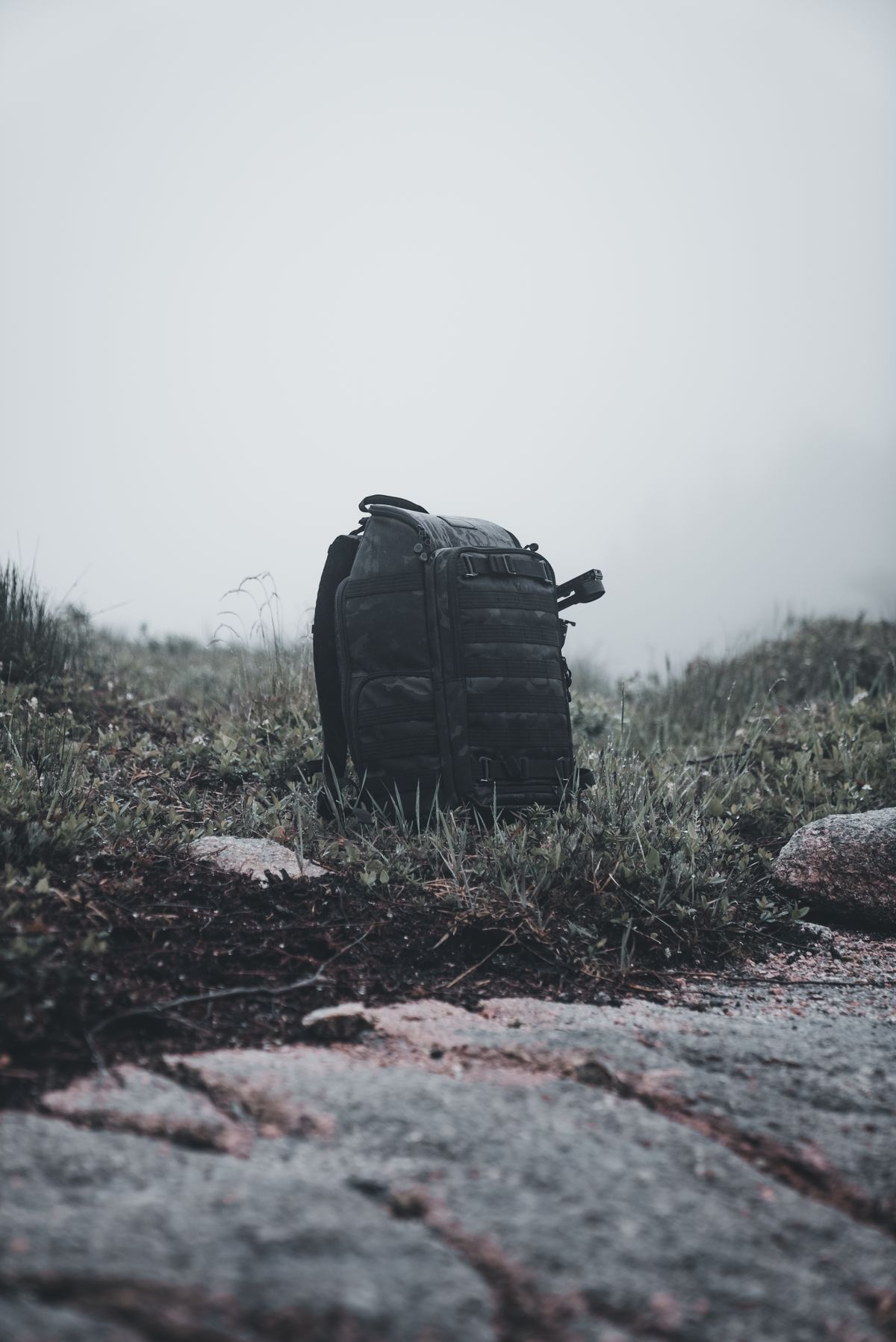 Dark hiking backpack resting on a misty hillside