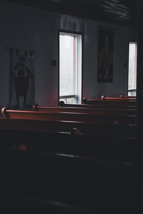 Free A moody church interior with rows of wooden pews and light filtering through windows. Stock Photo