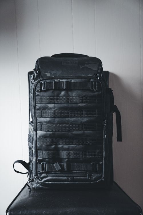 Free A durable black tactical backpack with straps and compartments, placed against a white wall. Stock Photo