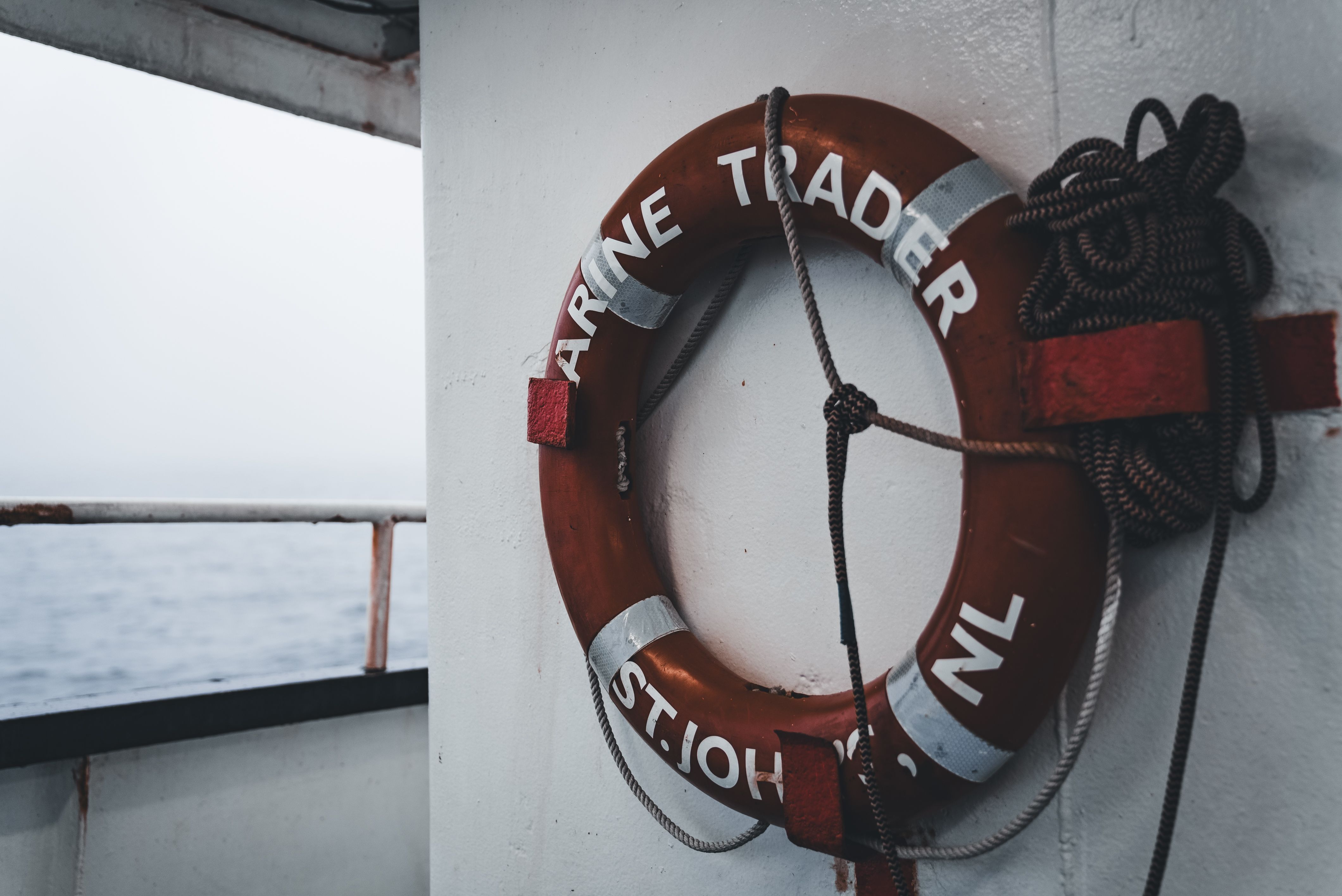 Red lifebuoy marked 'Marine Trader St. John's NL' hangs on a boat deck, symbolizing safety at sea.