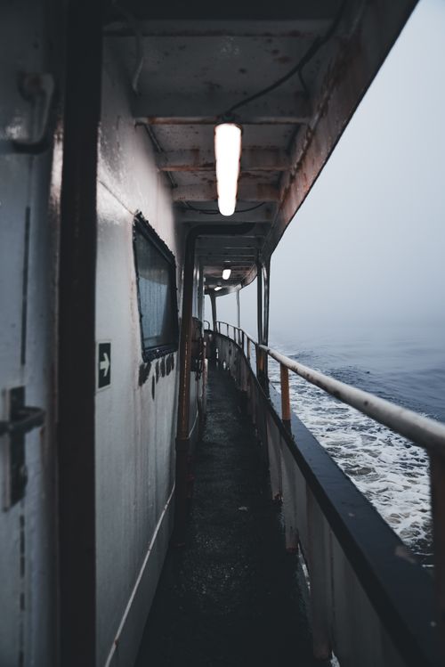 Free View of a ship's deck with metal railing, surrounded by fog over the sea, creating a moody ambiance. Stock Photo