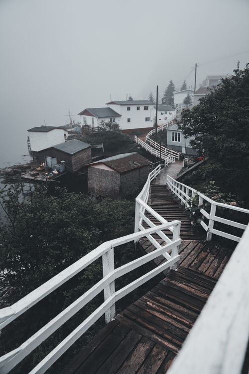 Free Misty view of a wooden footbridge leading through a foggy coastal town, creating a serene atmosphere. Stock Photo