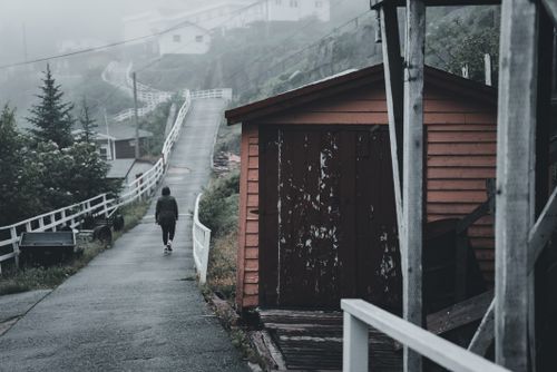 Free A lone figure walks down a foggy urban alley beside a rustic orange shed. Stock Photo