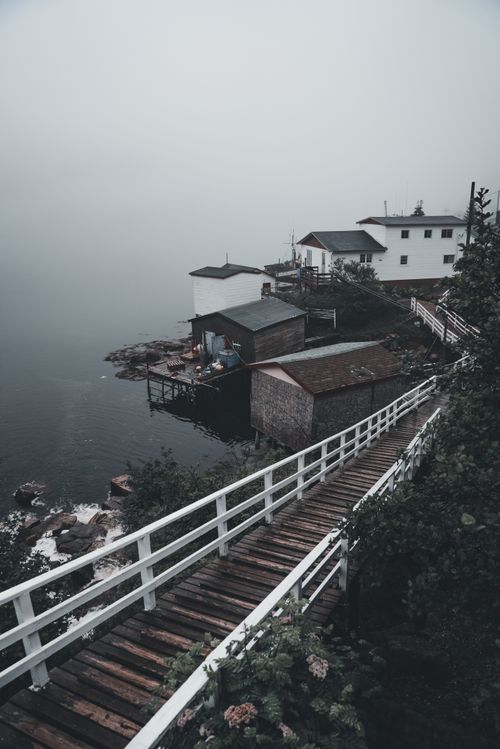 Free Serene view of a misty coastal town with a wooden footbridge leading to waterfront houses. Stock Photo