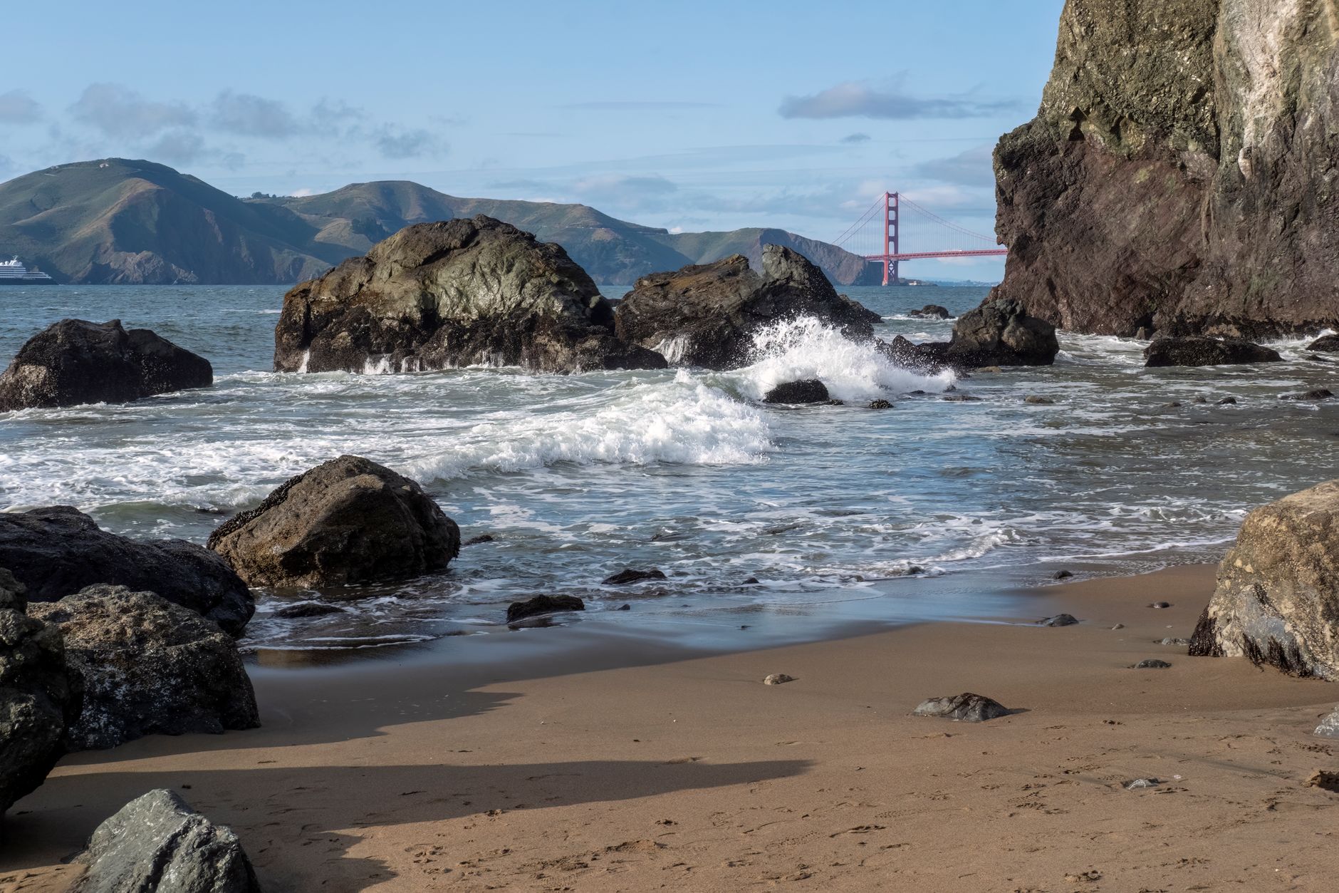 Scenic view of rocky shoreline with waves and the Golden Gate Bridge in the background.