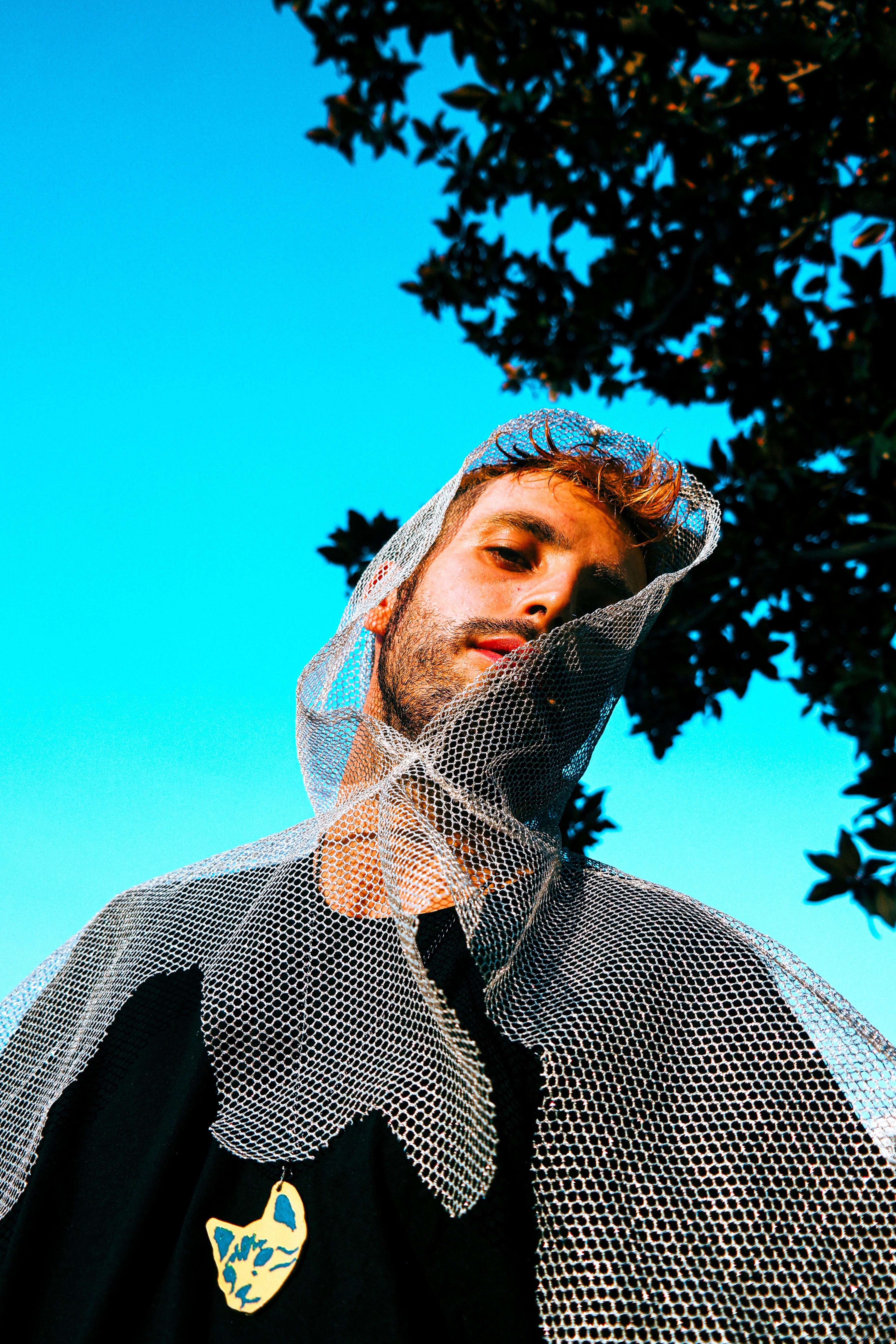 Creative outdoor portrait of a man with mesh cloth under a bright blue sky.