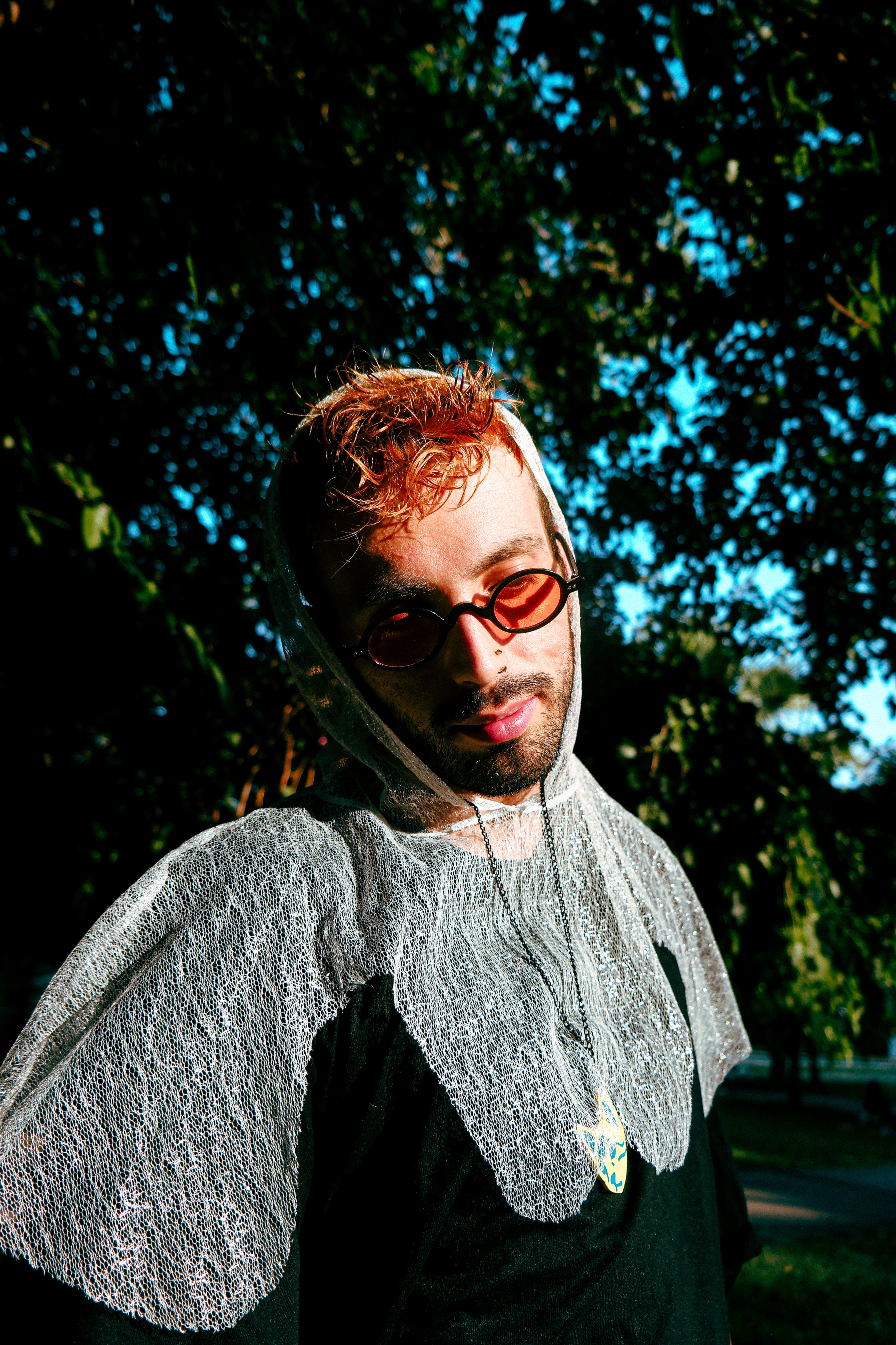 Fashion-forward man with a lace hood and sunglasses captured under natural light.