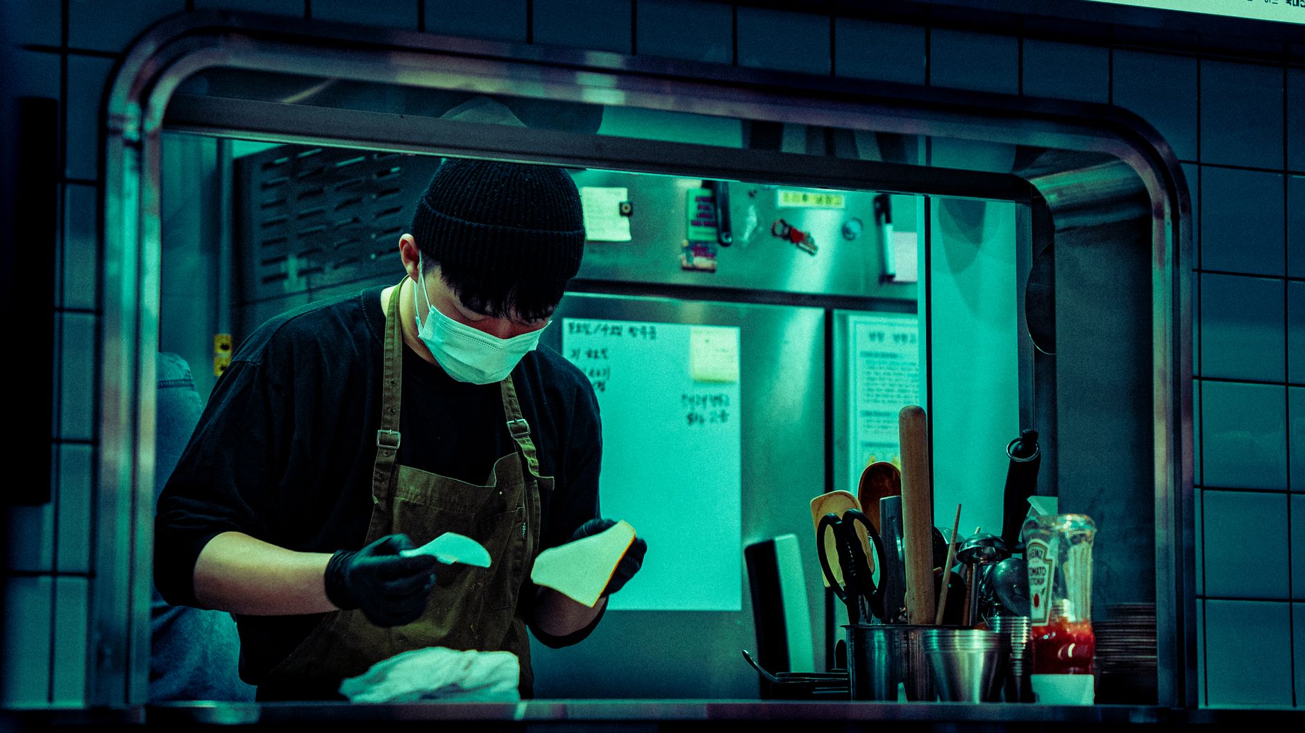 Masked chef working in an industrial kitchen, focused on food preparation.