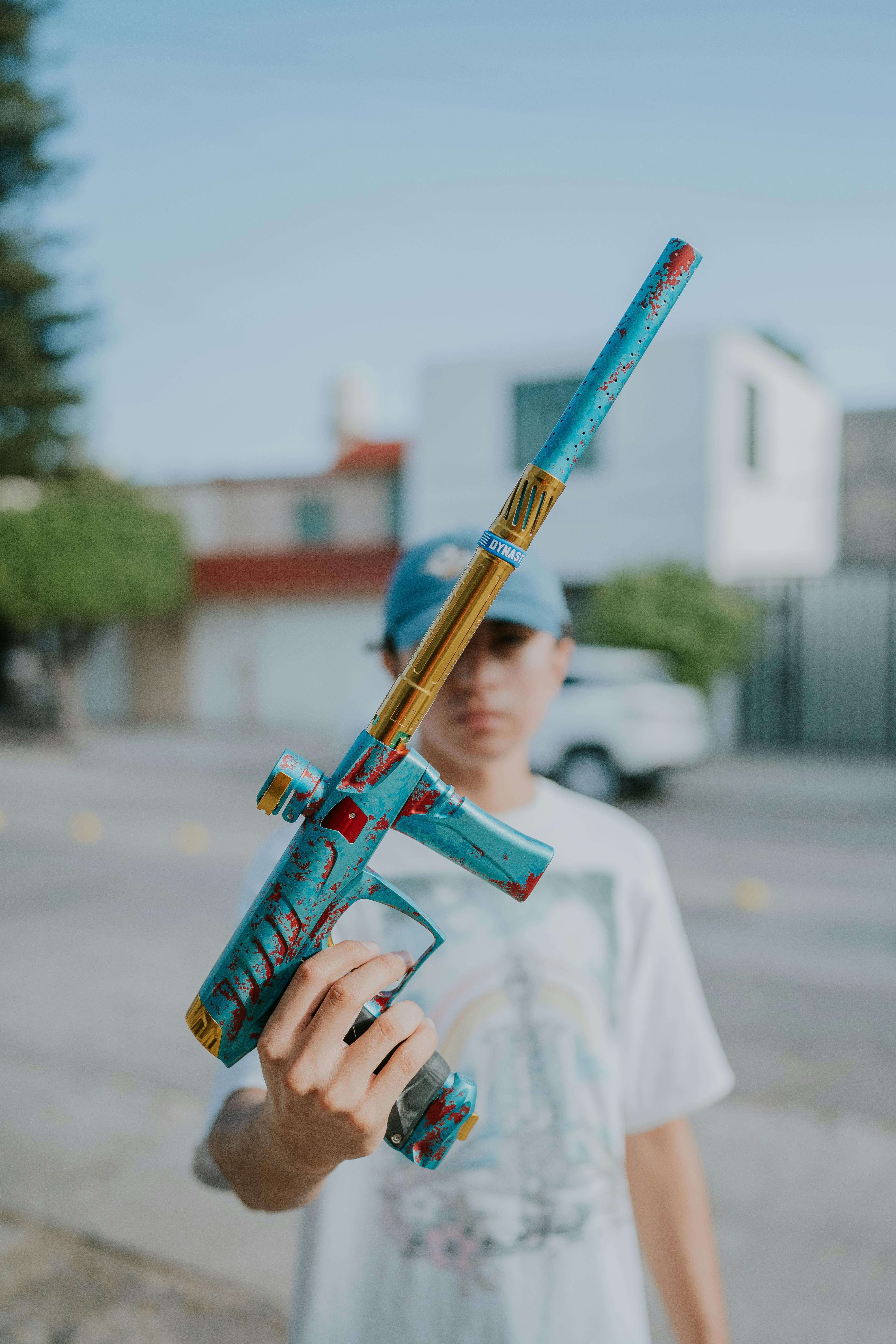 Ein Teenager hält im Freien in einer städtischen Umgebung ein Paintballgewehr und konzentriert sich auf die bunte Ausrüstung. Prescription Goggle Inserts - A teenager holding a paintball gun outdoors in an urban setting, focusing on the colorful equipment.