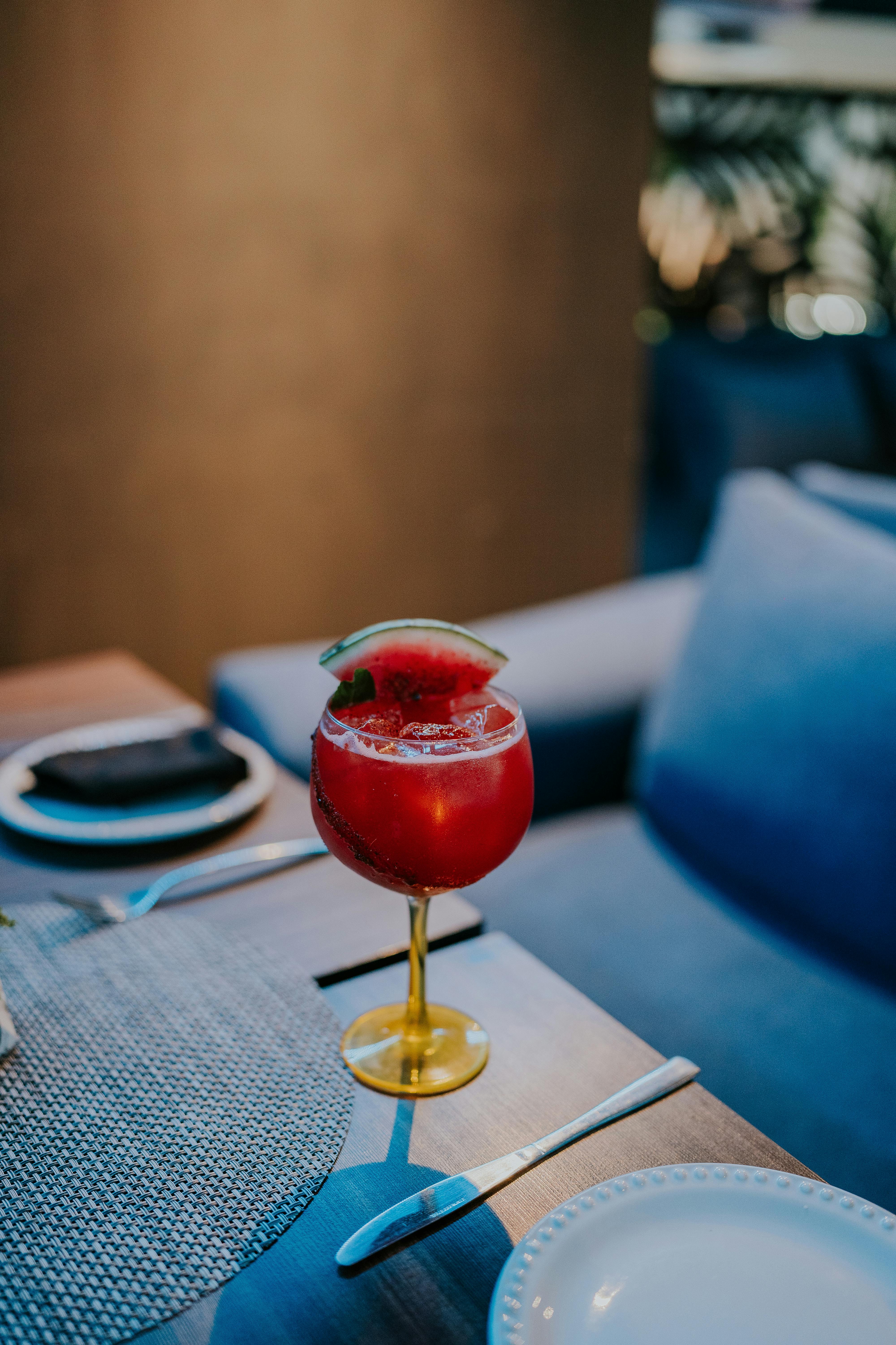 Elegant watermelon cocktail with a slice garnish served on a table setting in a cozy indoor environment.