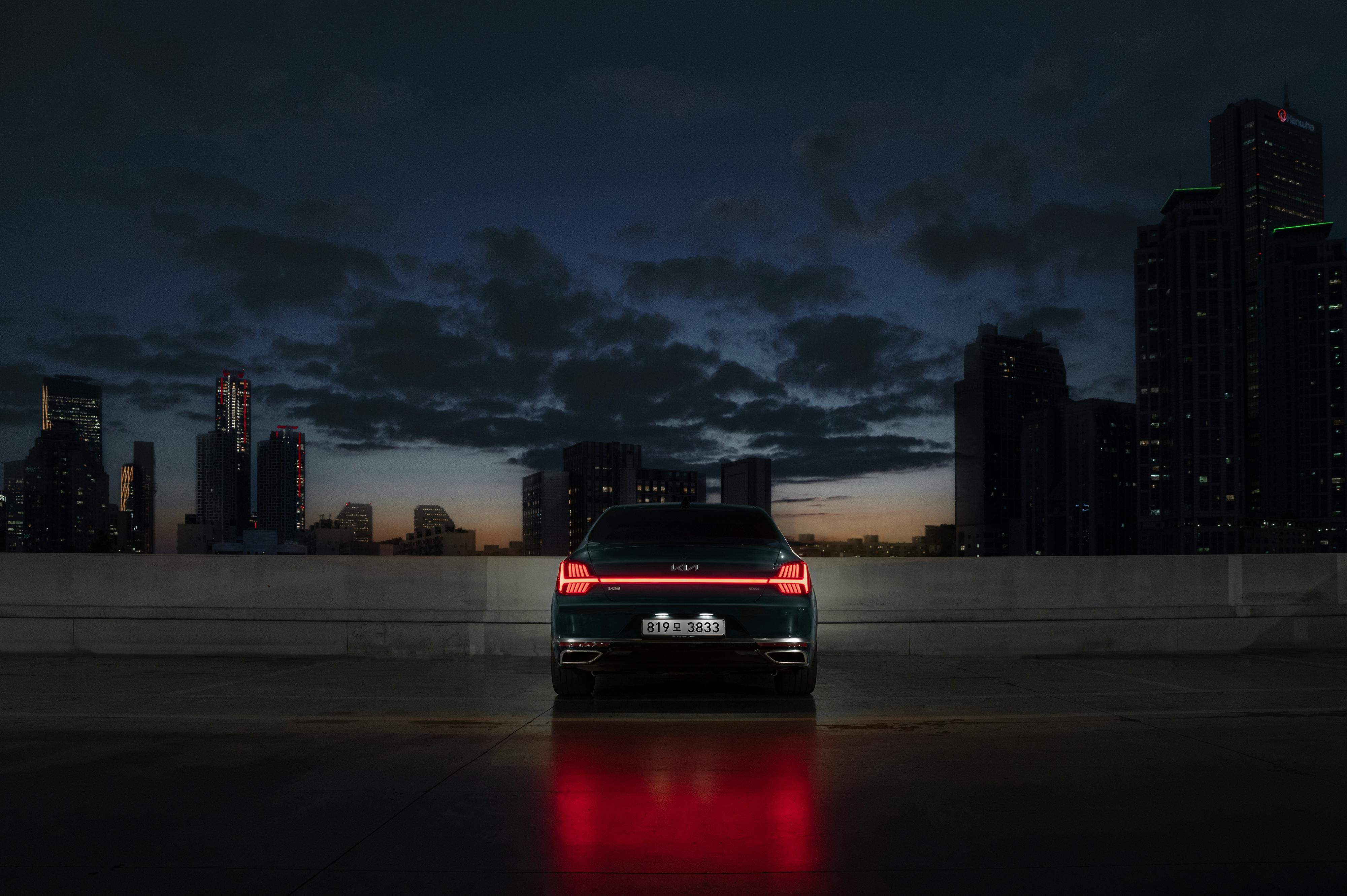 A car parked in a cityscape at twilight, highlighting its brake lights and skyline backdrop.