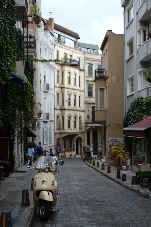 Free A picturesque narrow European alley lined with historic buildings and a classic scooter parked on cobblestones. Stock Photo