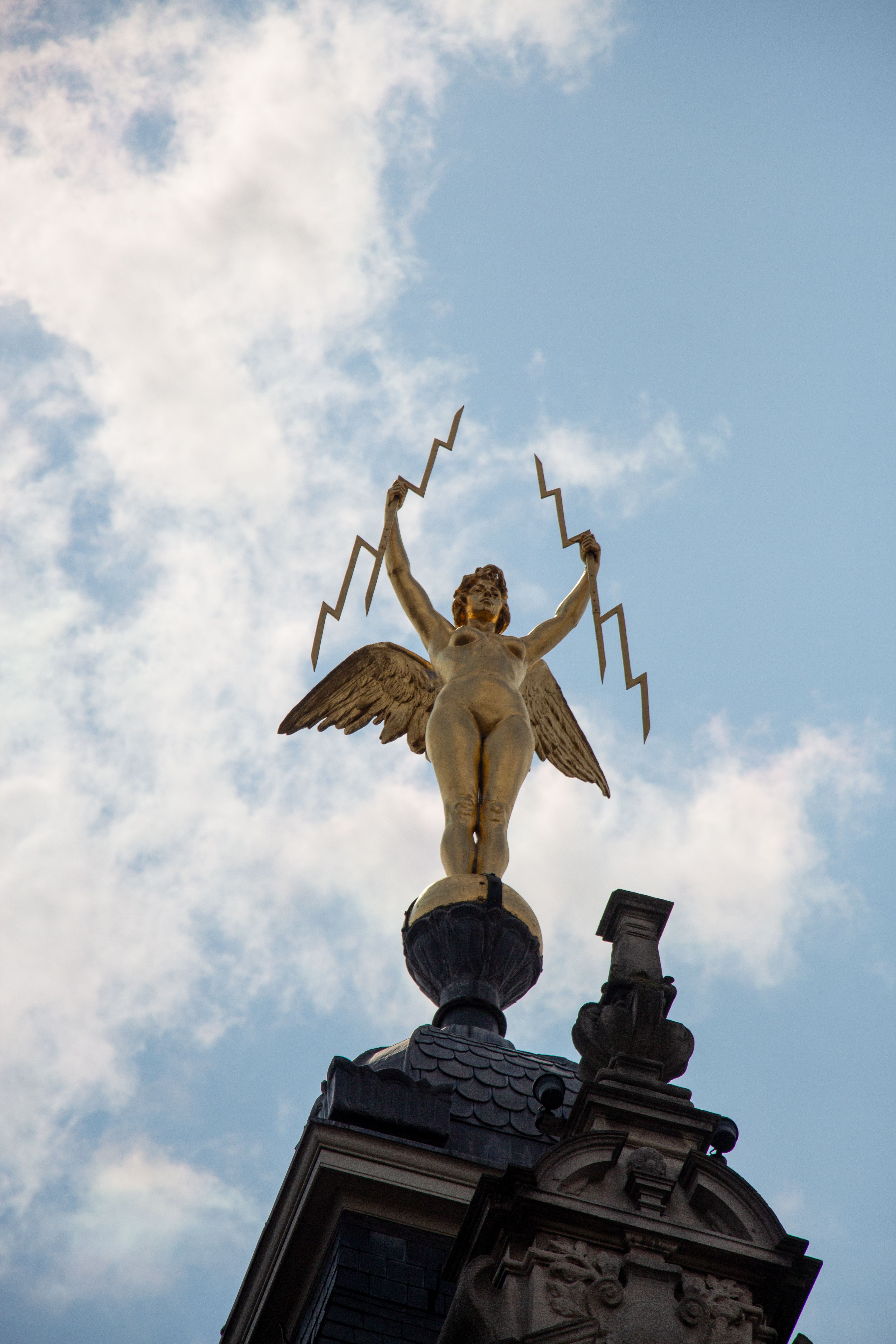 A striking golden angel statue holding lightning bolts against the sky in Antwerp, Belgium.
