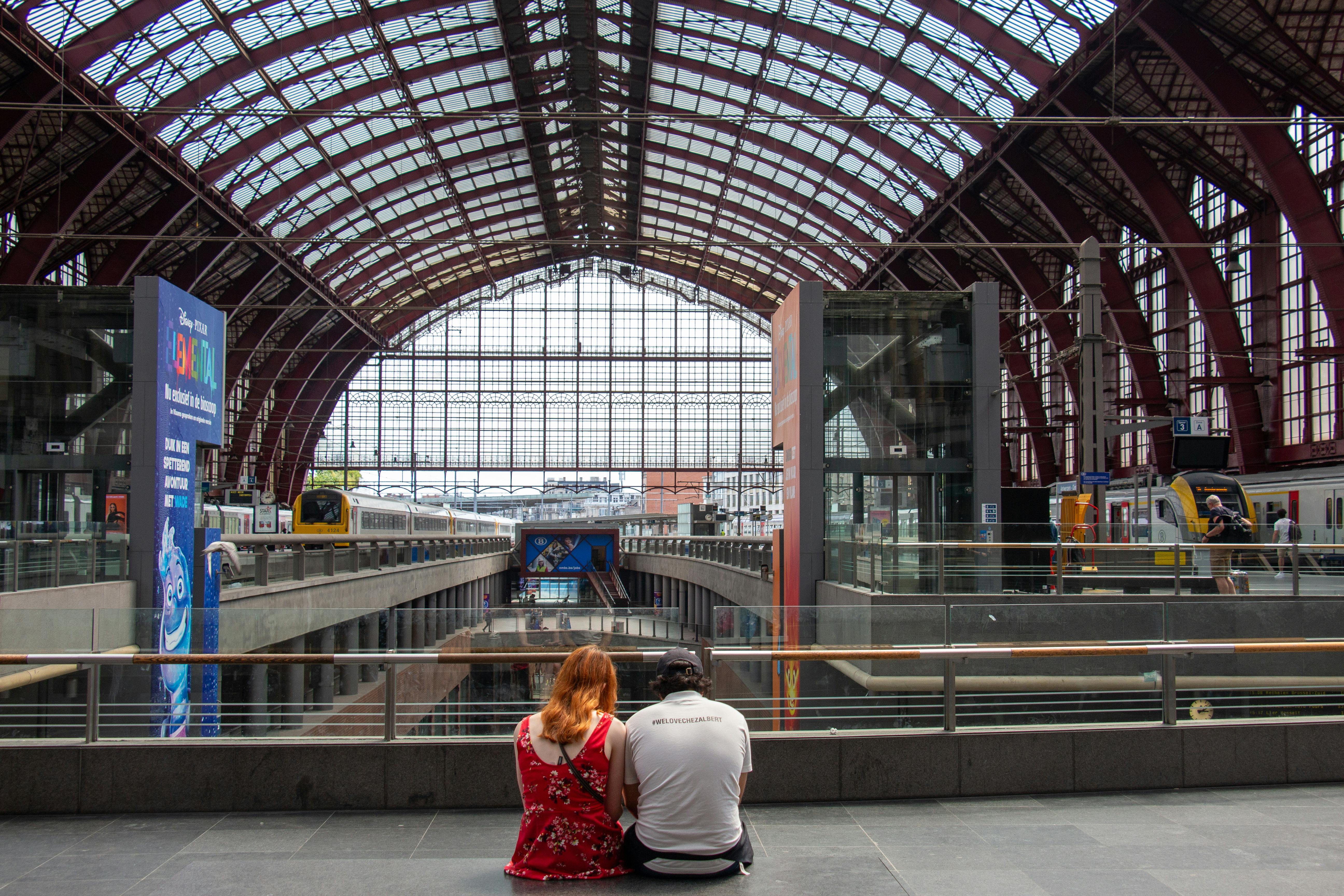A couple sits at Antwerp Central Station in Belgium, showcasing its architectural beauty.