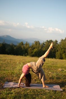 Woman practicing yoga outdoors on a mat, balancing in a scenic mountain meadow.