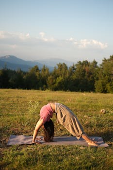 Woman performing yoga in a serene outdoor setting with a scenic view of mountains and trees.