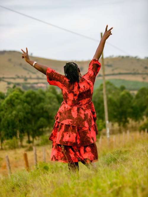 Woman in Red Dress Standing with Arms Raised on Grassland