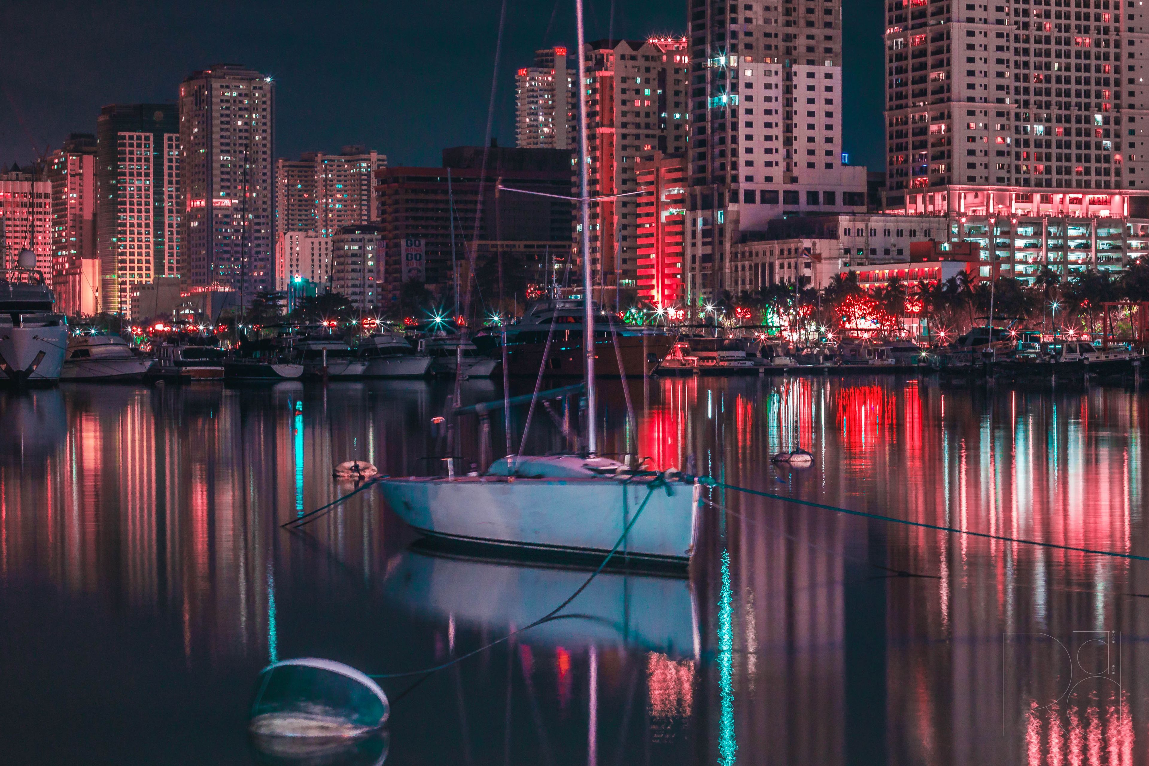 A vibrant cityscape at night featuring illuminated buildings and a calm marina with reflections.