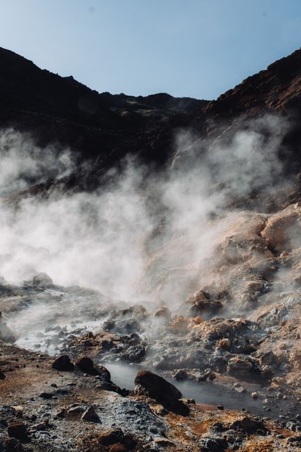 Dramatic view of a steaming geothermal landscape with rocky terrain.